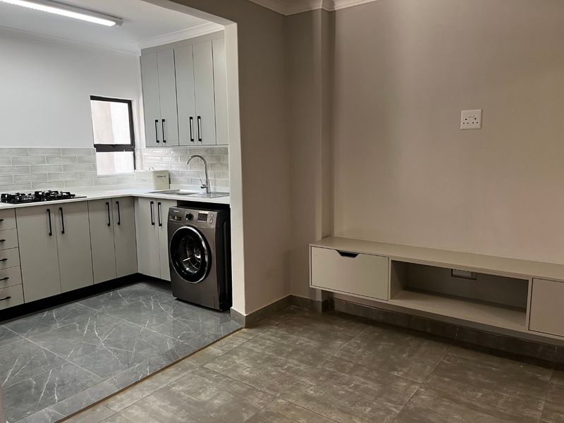 Modern open-plan kitchen and living area featuring sleek cabinetry, gas hob, tiled floors, and a built-in floating media console.