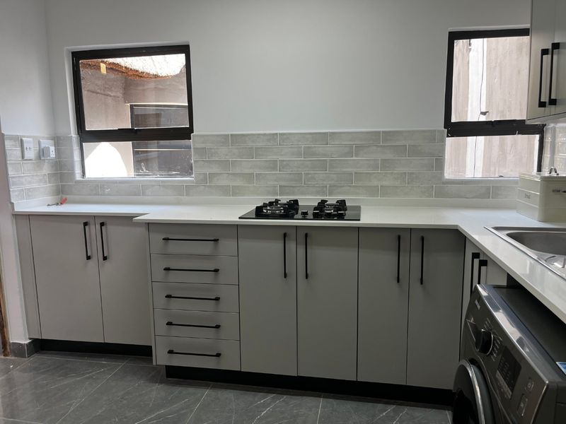 Modern kitchen featuring light grey cabinetry, stone countertops, a gas hob, subway tile backsplash, and sleek black hardware.