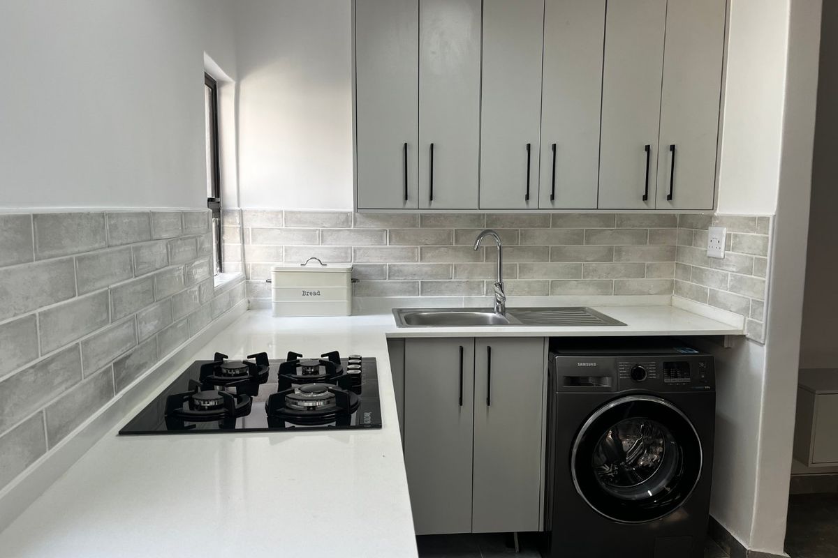 Modern kitchen featuring light grey cabinetry, subway tile backsplash, quartz countertops, integrated gas hob, and a stainless steel sink.
