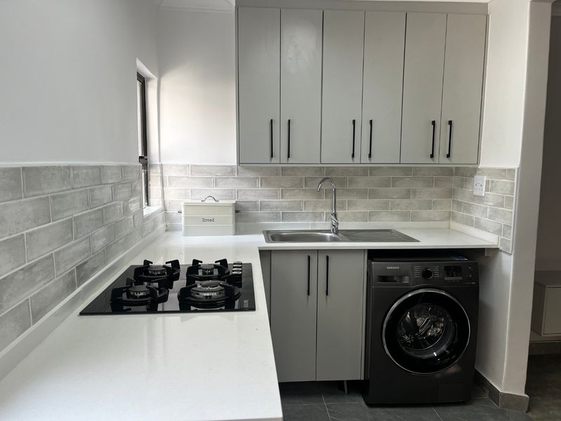 Modern kitchen featuring light grey cabinetry, subway tile backsplash, quartz countertops, integrated gas hob, and a stainless steel sink.
