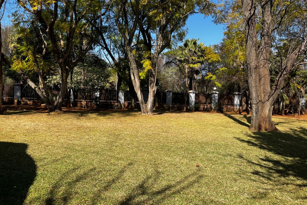 A spacious, well-maintained garden featuring mature trees and a secure boundary wall with concrete pillars.