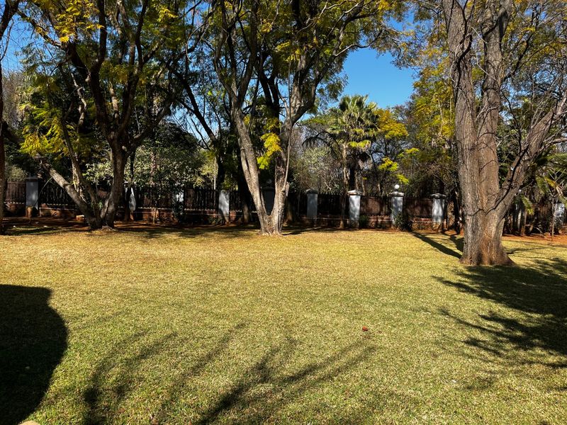 A spacious, well-maintained garden featuring mature trees and a secure boundary wall with concrete pillars.