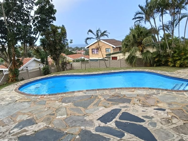 Outdoor pool area featuring a swimming pool surrounded by stone paving and a perimeter wall, set within a landscaped garden.