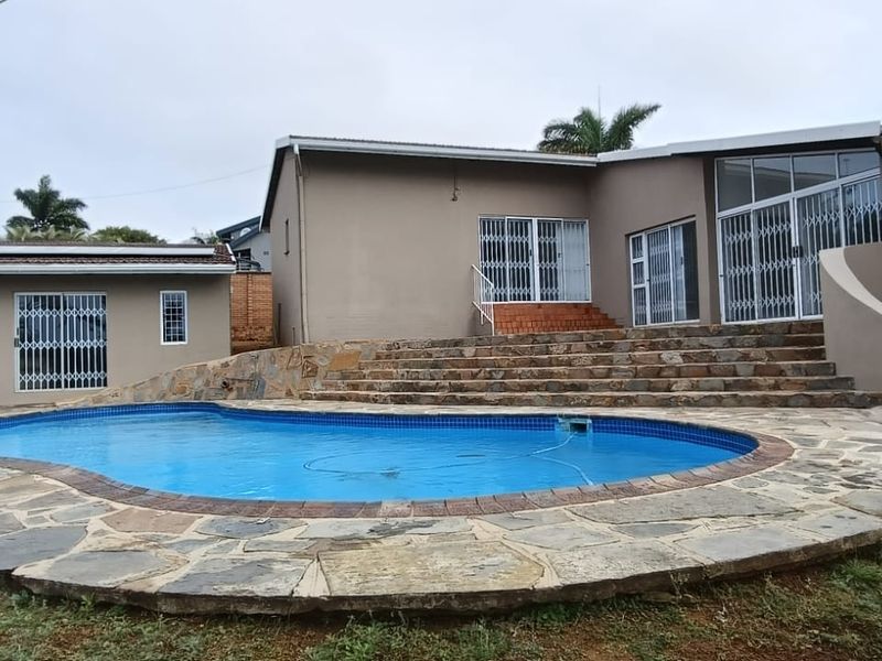 Rear exterior view featuring a swimming pool with stone paving, stone stairs leading to the house, and multiple sliding door access points.