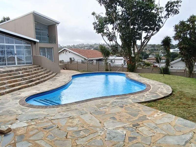 Outdoor pool area featuring a kidney-shaped swimming pool, stone-paved patio, and direct access to the rear of the house.