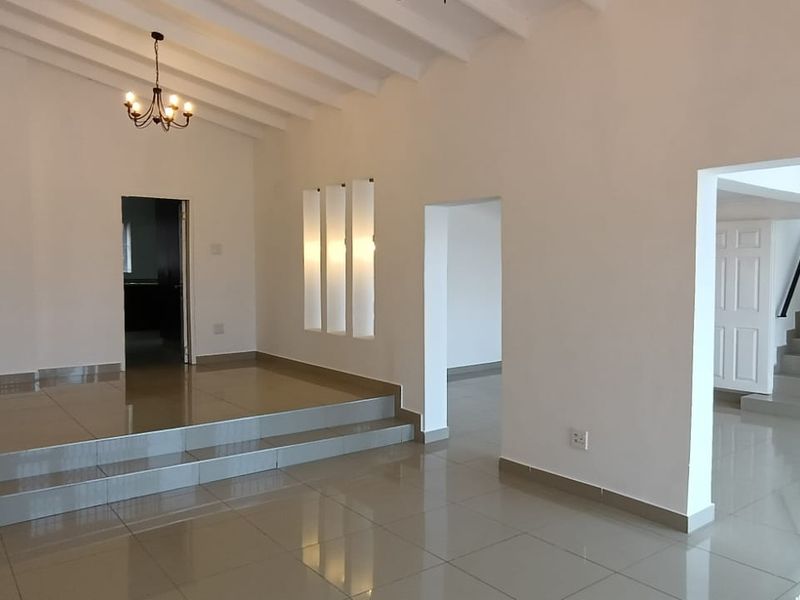 Spacious, open-plan living area featuring polished tiled floors, a raised platform, exposed beam ceilings, and a staircase leading to the upper level.