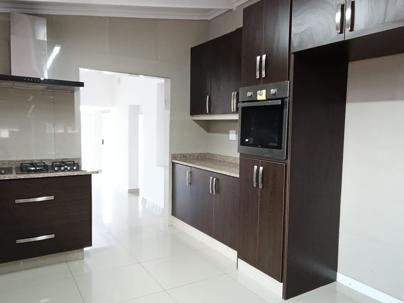 A modern, empty kitchen featuring dark wood cabinetry, laminate countertops, a gas hob, extractor fan, and built-in oven with tiled flooring.