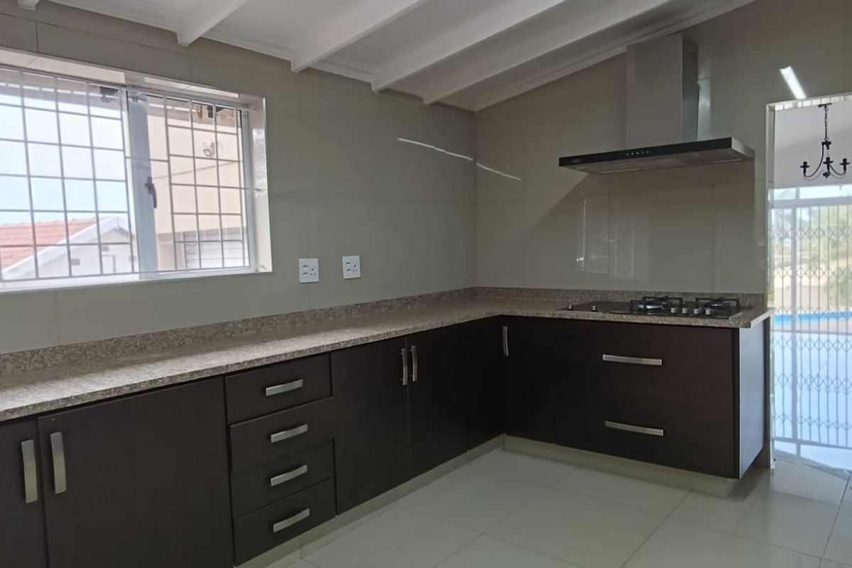 Modern kitchen featuring dark cabinetry, granite countertops, a gas hob with extractor fan, and tiled flooring, offering a clean and functional workspace.