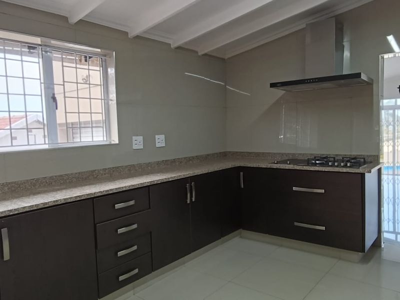 Modern kitchen featuring dark cabinetry, granite countertops, a gas hob with extractor fan, and tiled flooring, offering a clean and functional workspace.