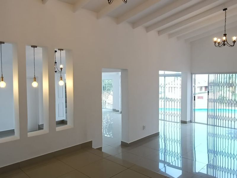 Spacious, light-filled living area featuring high exposed beam ceilings, tiled flooring, and decorative wall niches, with direct access to the outdoor pool area.