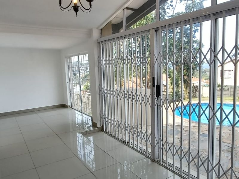 Spacious, light-filled living area featuring large sliding glass doors with security gates, tiled flooring, and direct access to the outdoor pool area.