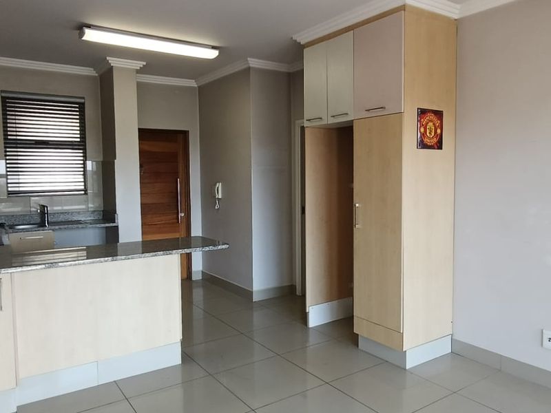 An open-plan kitchen and living area featuring light wood cabinetry, granite countertops, and neutral ceramic floor tiles in a clean, vacant space.