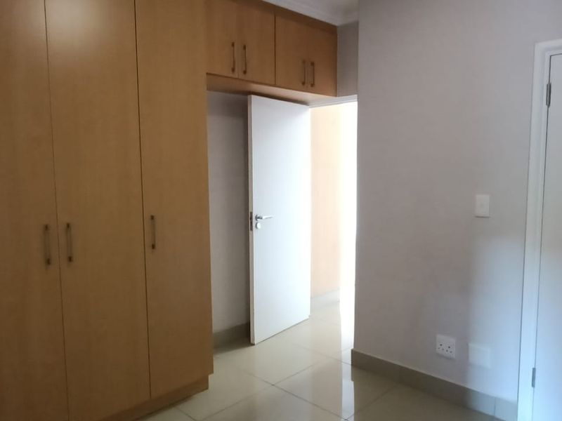 A clean, empty bedroom featuring light-toned built-in cupboards, neutral tiled flooring, and white internal doors.