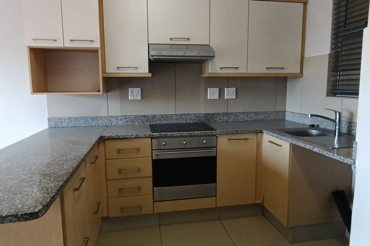 A functional kitchen featuring granite countertops, built-in oven, electric hob, extractor fan, and ample laminate cabinetry with a breakfast bar extension.