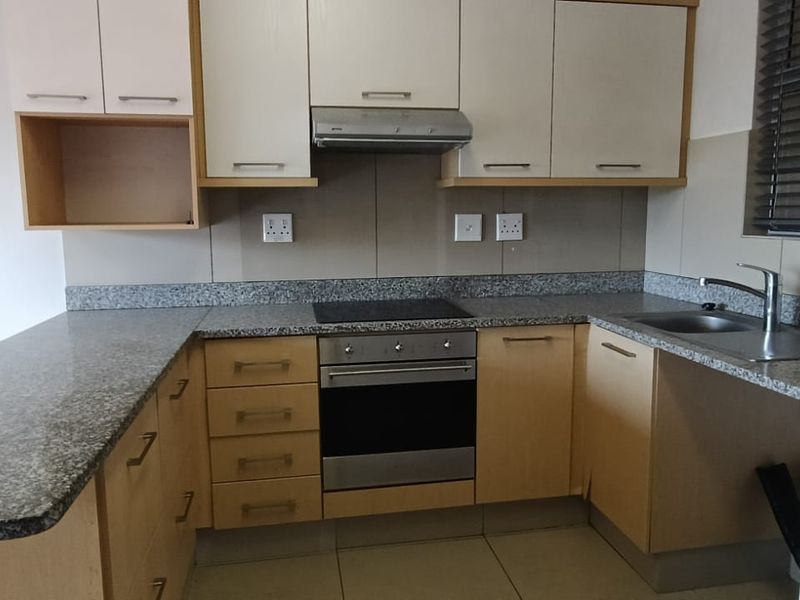 A functional kitchen featuring granite countertops, built-in oven, electric hob, extractor fan, and ample laminate cabinetry with a breakfast bar extension.