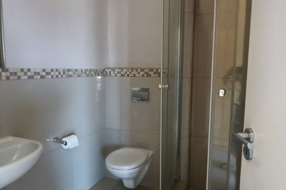 A clean, functional bathroom featuring a wall-mounted toilet, glass shower enclosure, and a pedestal basin with modern chrome fixtures.