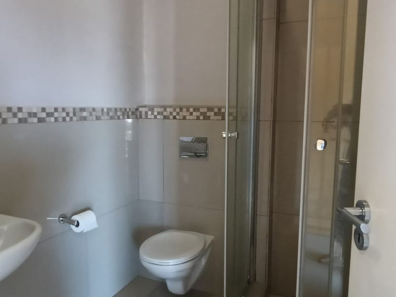 A clean, functional bathroom featuring a wall-mounted toilet, glass shower enclosure, and a pedestal basin with modern chrome fixtures.
