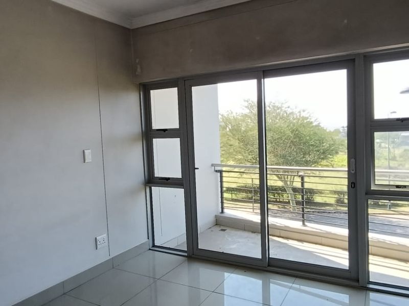 An empty bedroom featuring tiled flooring and a large sliding glass door providing access to a private balcony.