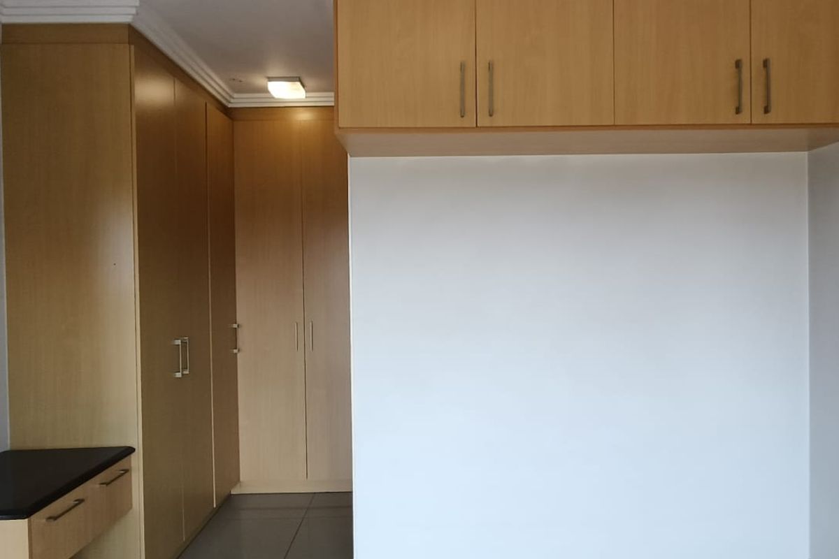 A clean, empty bedroom featuring extensive light wood built-in cabinetry, overhead storage, a built-in vanity, and neutral tiled flooring.