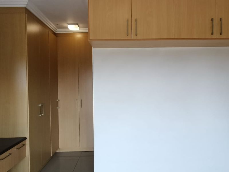 A clean, empty bedroom featuring extensive light wood built-in cabinetry, overhead storage, a built-in vanity, and neutral tiled flooring.