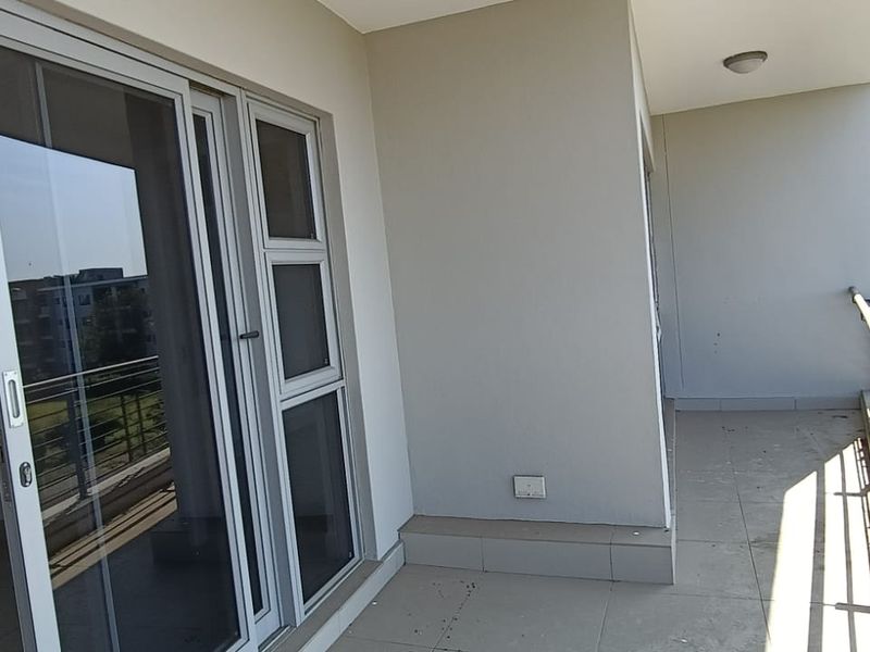 A spacious covered balcony featuring tiled flooring, a metal balustrade, and direct access to the interior through a large sliding glass door.