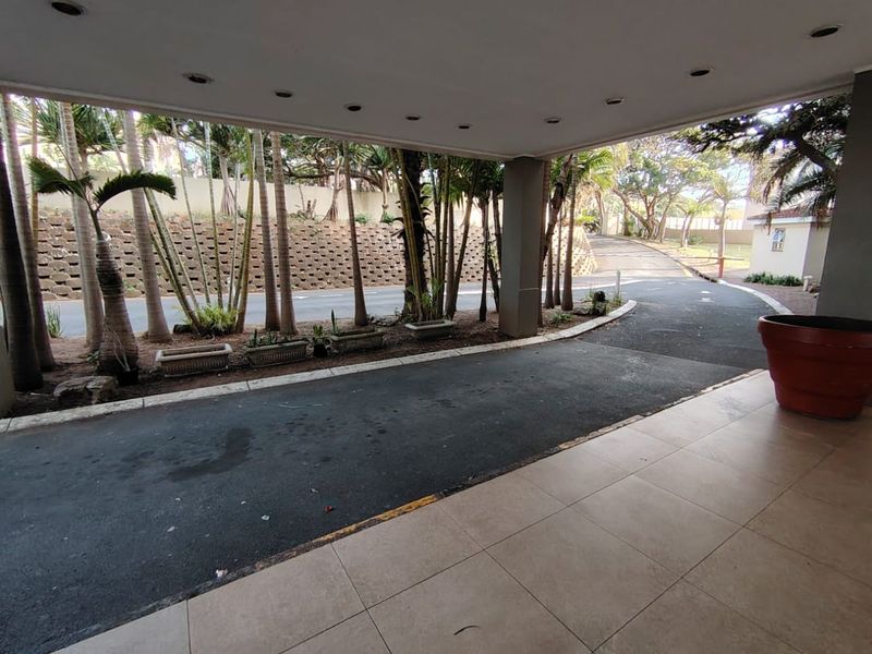 A covered driveway entrance featuring tiled flooring, recessed ceiling lights, and a landscaped retaining wall area.
