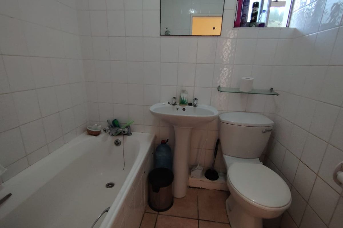 A functional bathroom featuring a pedestal basin, bathtub, and toilet with white wall tiling and tiled flooring.