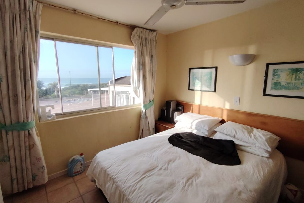 A bedroom featuring tiled flooring, a ceiling fan, and a large sliding window with ocean views, requiring cosmetic updates to the walls and finishes.