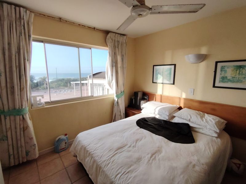 A bedroom featuring tiled flooring, a ceiling fan, and a large sliding window with ocean views, requiring cosmetic updates to the walls and finishes.