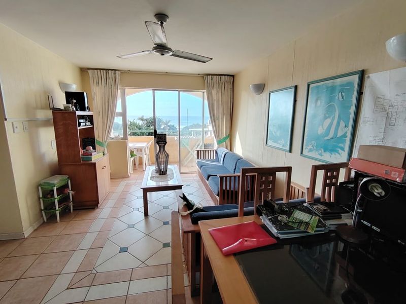 Open plan living area featuring ceramic tiled flooring, ceiling fan, and sliding glass doors leading to a balcony with ocean views.