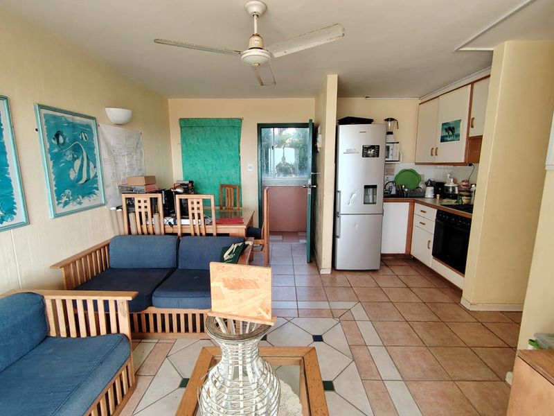 Open-plan living and kitchen area featuring tiled flooring, built-in cabinetry, and a ceiling fan, offering a functional layout with potential for modern updates.