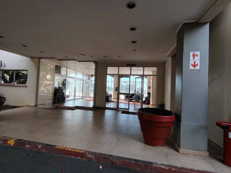 Covered entrance area featuring tiled flooring, glass doors, and recessed lighting, providing access to the building interior.