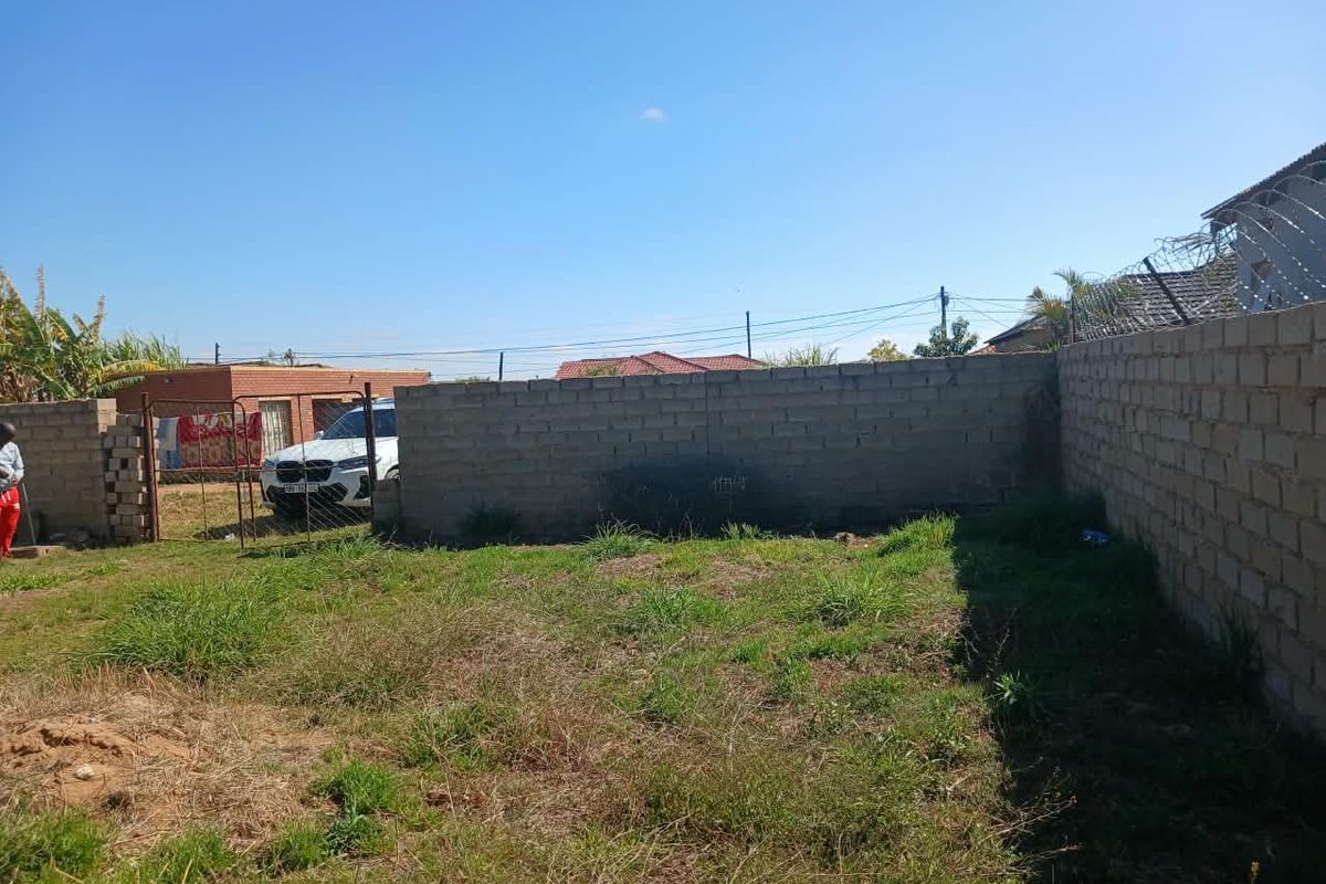 A rear yard area featuring an unfinished perimeter wall with security razor wire and a metal gate entrance.