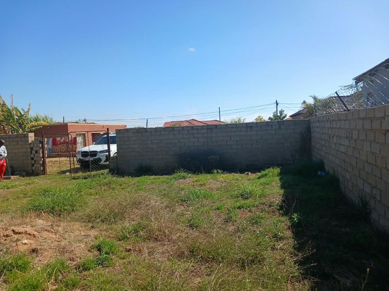 A rear yard area featuring an unfinished perimeter wall with security razor wire and a metal gate entrance.