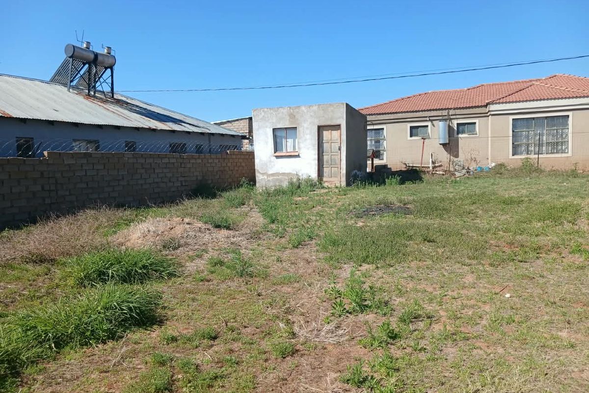 Rear yard view featuring an outbuilding, brick boundary wall with razor wire, and a solar water heater installed on the main house roof.