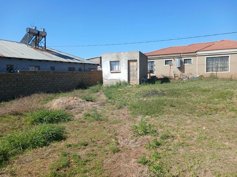 Rear yard view featuring an outbuilding, brick boundary wall with razor wire, and a solar water heater installed on the main house roof.