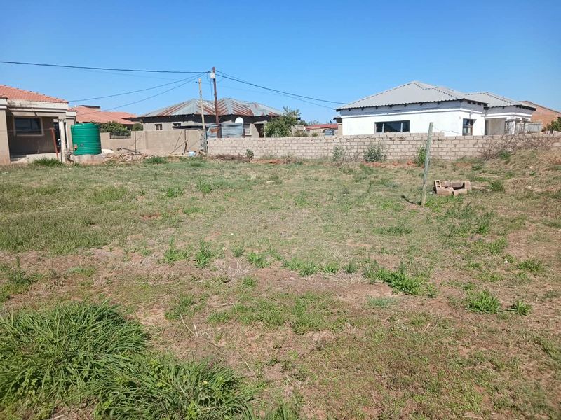 A spacious, undeveloped residential plot featuring a boundary wall and an existing water tank, offering potential for landscaping or future expansion.
