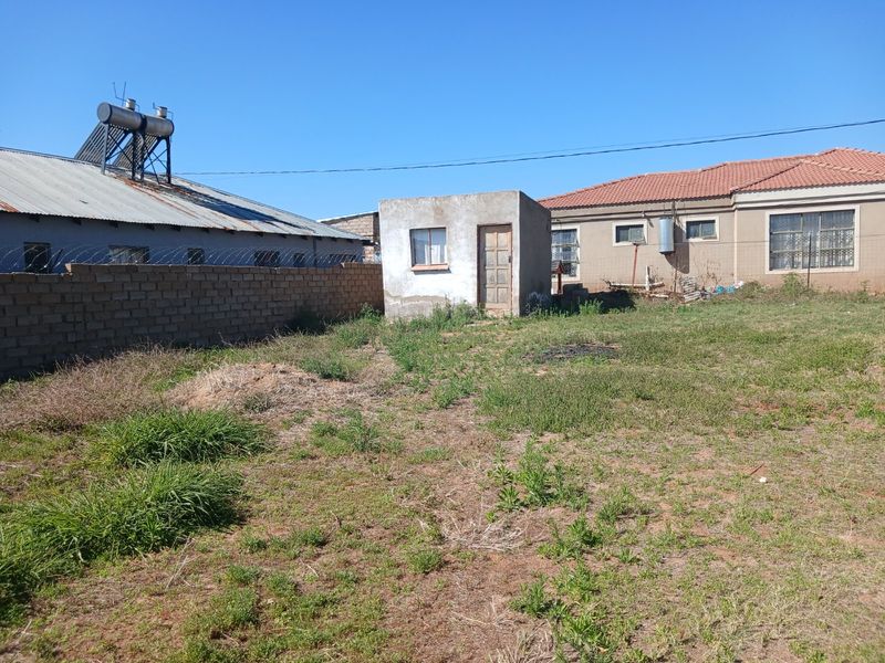 Rear yard view featuring a small outbuilding, brick boundary wall with security fencing, and a solar water heating system on the main roof.