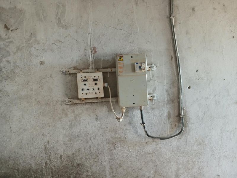 A utility wall featuring an exposed electrical distribution board and socket with visible surface wear and plaster cracking.