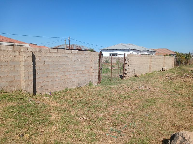 A view of the property boundary featuring a concrete block wall and a damaged metal gate entrance.