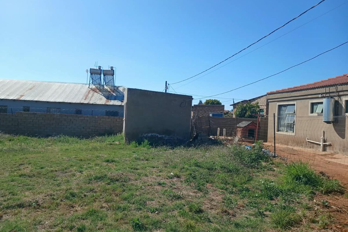 Rear yard area featuring a boundary wall, wire fencing, and an external geyser unit with a solar water heater visible on the roof.