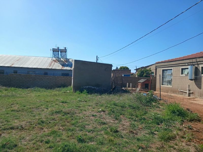 Rear yard area featuring a boundary wall, wire fencing, and an external geyser unit with a solar water heater visible on the roof.