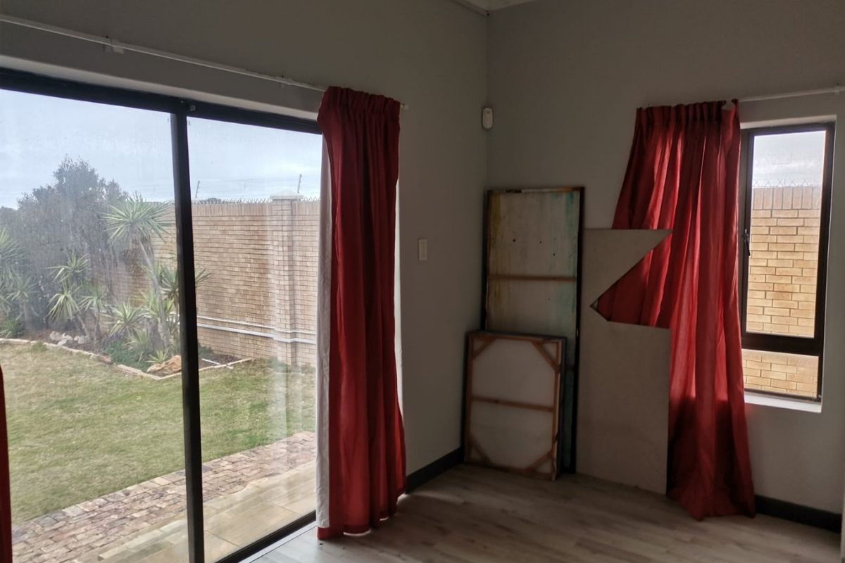 A bright, empty living room featuring laminate flooring, a large sliding glass door, and a window with views of the rear garden.