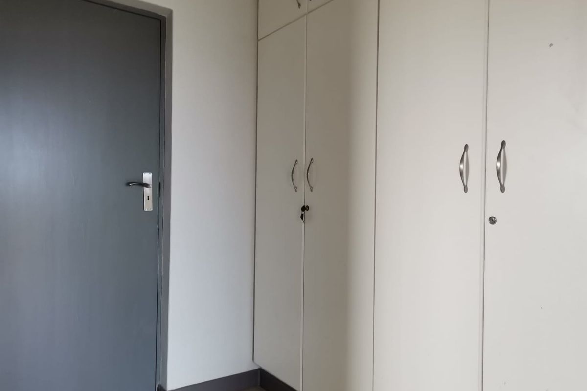A clean, empty bedroom featuring neutral walls, light wood-look flooring, and ample built-in cupboard storage with modern hardware.