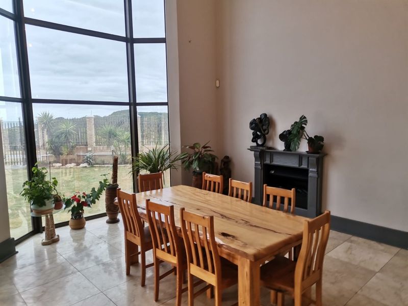 Spacious dining area featuring large floor-to-ceiling windows, tiled flooring, and a built-in fireplace, offering ample natural light and garden views.