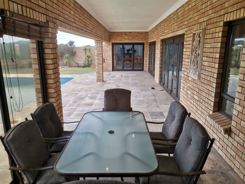 A spacious covered patio featuring exposed brick walls, stone tile flooring, and recessed lighting, providing seamless access to the garden and pool area.