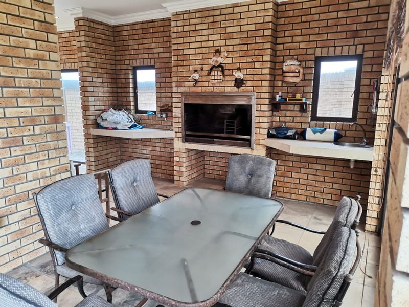 Covered patio area featuring a built-in brick braai, concrete prep counters, and a sink, providing a functional outdoor entertainment space.