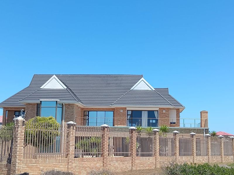 A well-maintained double-story brick house featuring a tiled roof, large aluminium windows, and a secure perimeter wall with metal fencing.