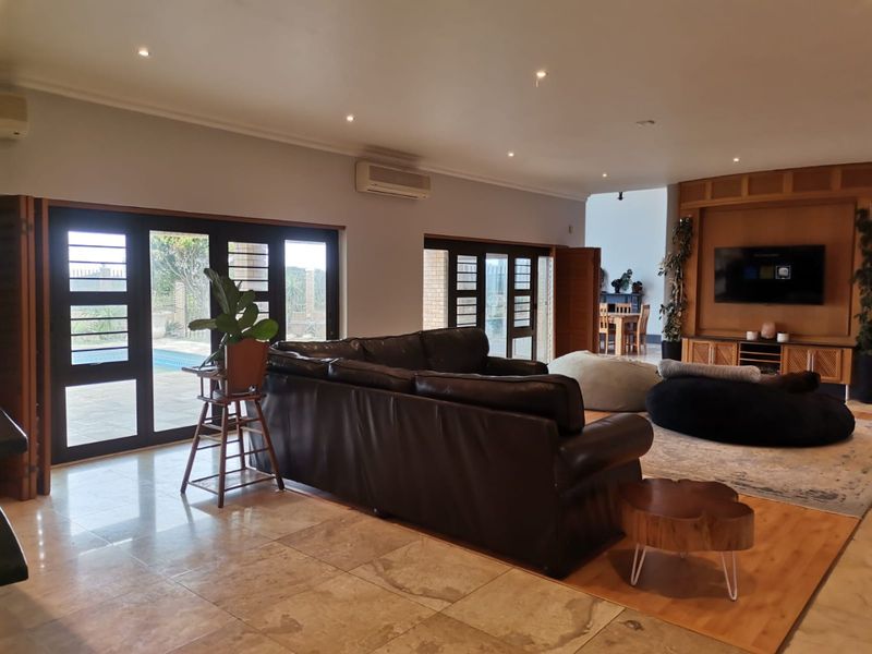 Spacious open-plan living area featuring stone flooring, built-in timber media cabinetry, and large glass doors providing direct access to the outdoor pool area.