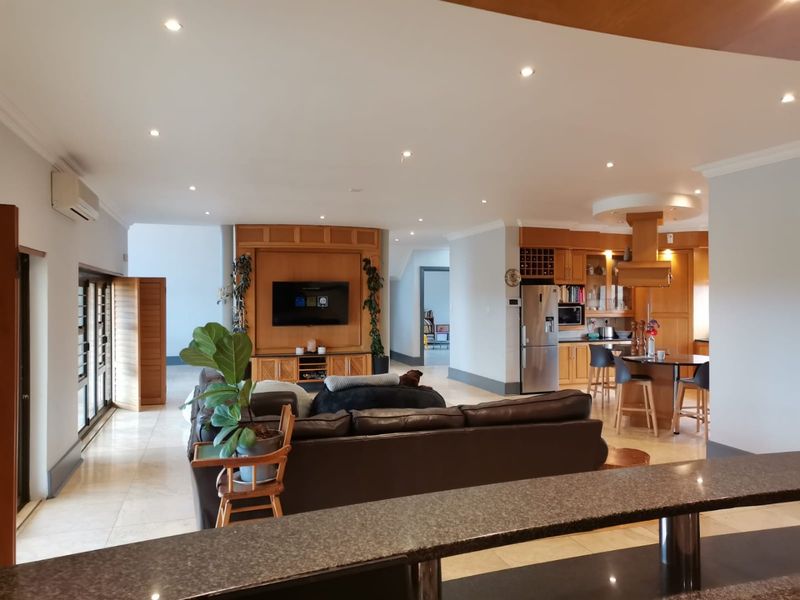Spacious open-plan living area featuring a modern kitchen with stone countertops, breakfast bar, and integrated cabinetry, flowing into a comfortable lounge space.
